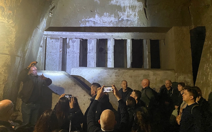 People exploring ancient walls during a guided tour in Naples underground.