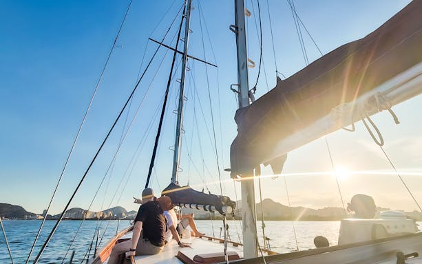 Tourists on sailboat enjoying Rio de Janeiro skyline at sunset.