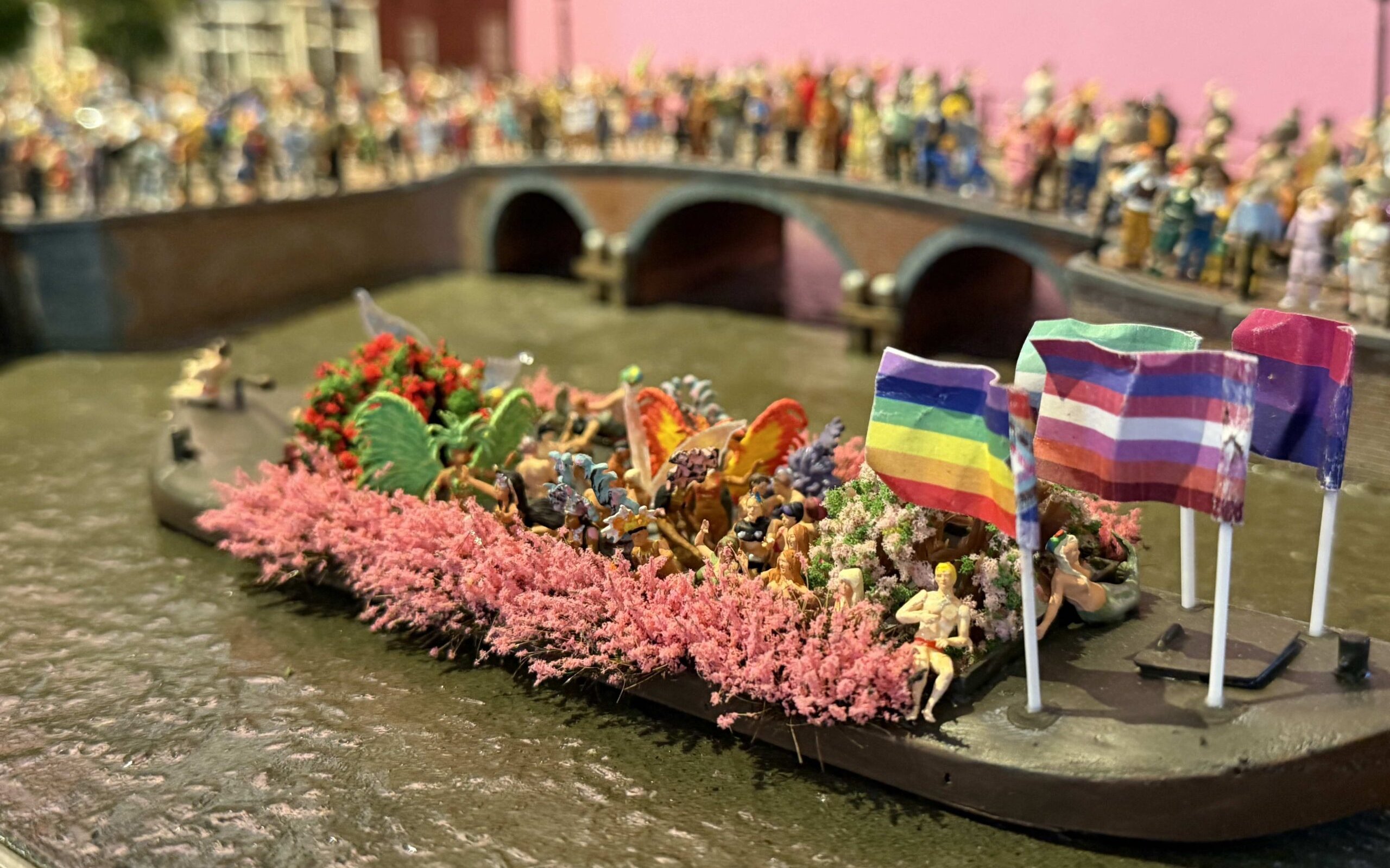 Canal boat with rainbow flags and people celebrating Pride Amsterdam.