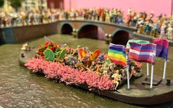 Canal boat with rainbow flags and people celebrating Pride Amsterdam.