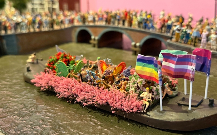 Canal boat with rainbow flags and people celebrating Pride Amsterdam.