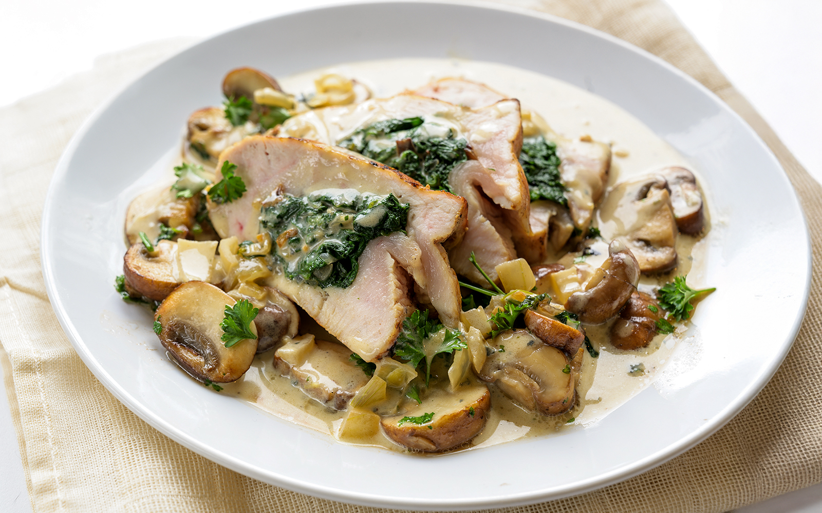 Stuffed chicken breast with spinach, mushrooms, and gorgonzola sauce on a white plate.