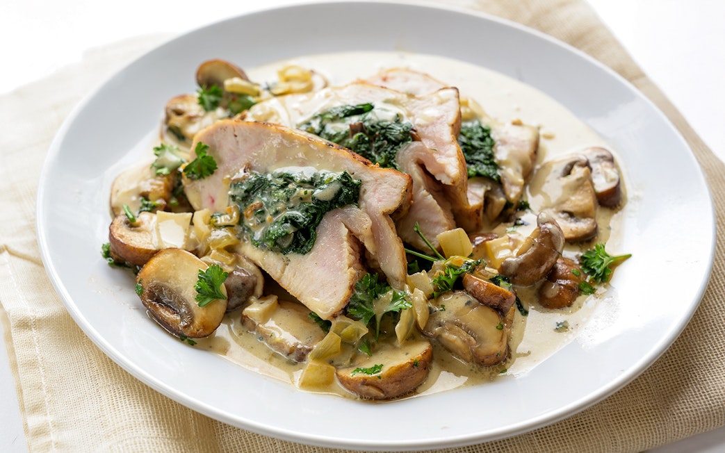 Stuffed chicken breast with spinach, mushrooms, and gorgonzola sauce on a white plate.