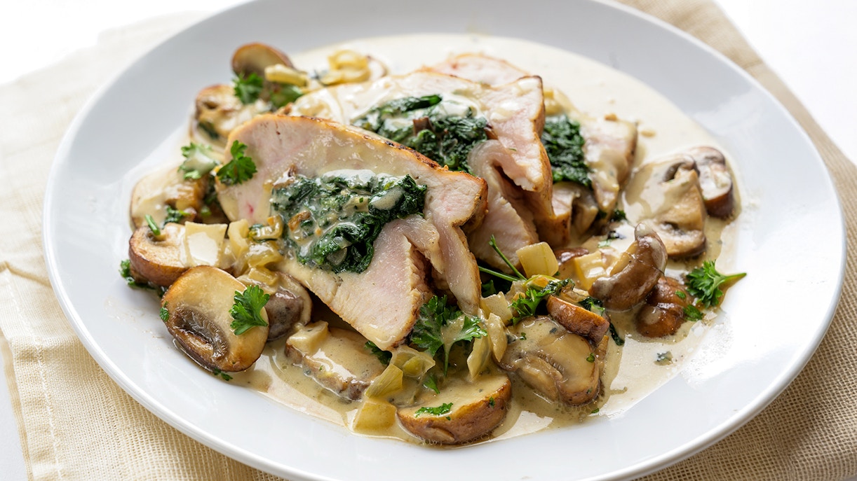 Stuffed chicken breast with spinach, mushrooms, and gorgonzola sauce on a white plate.