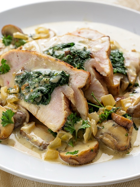 Stuffed chicken breast with spinach, mushrooms, and gorgonzola sauce on a white plate.