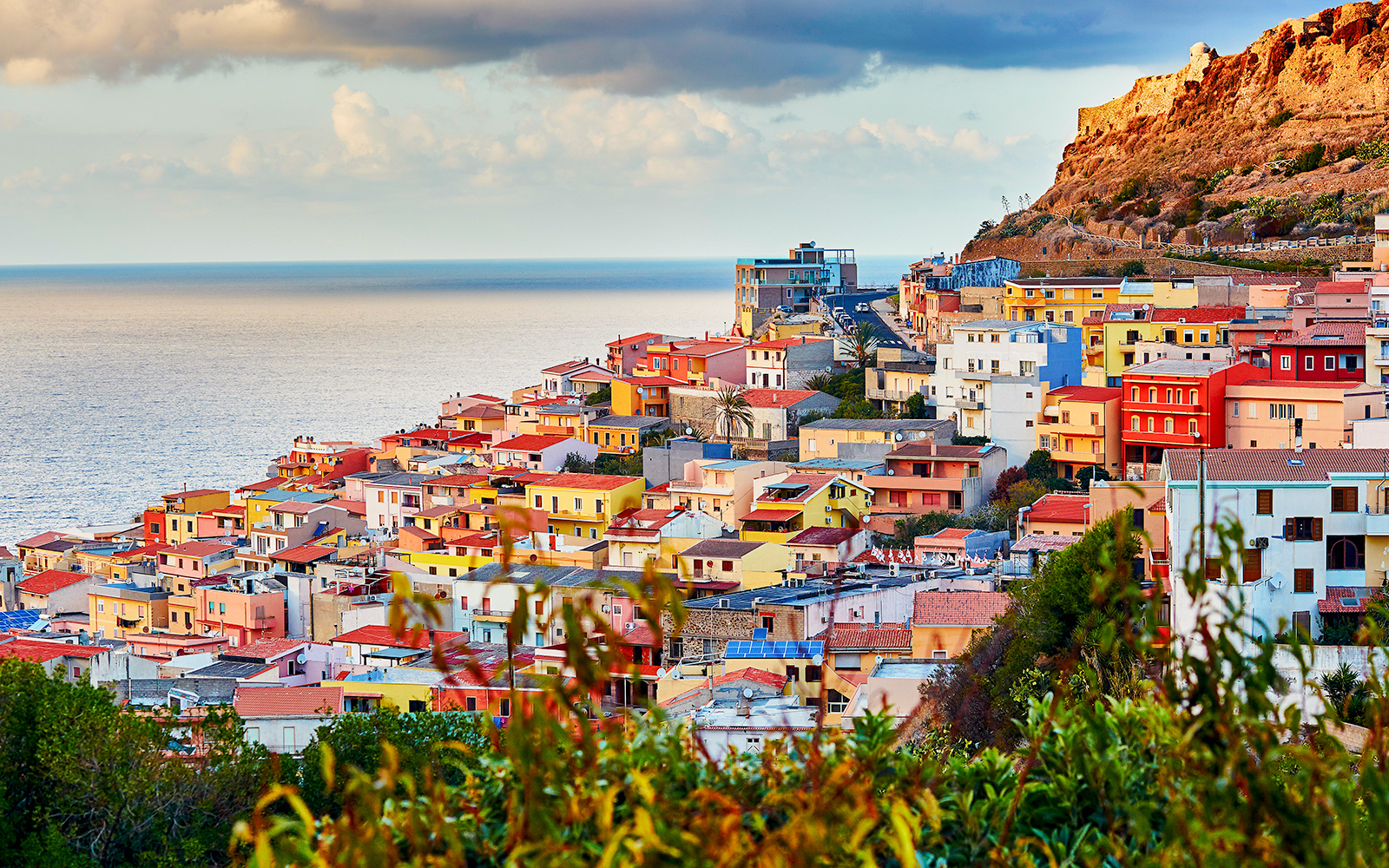 Sardinia cityscape at sunset with historic buildings and coastline.