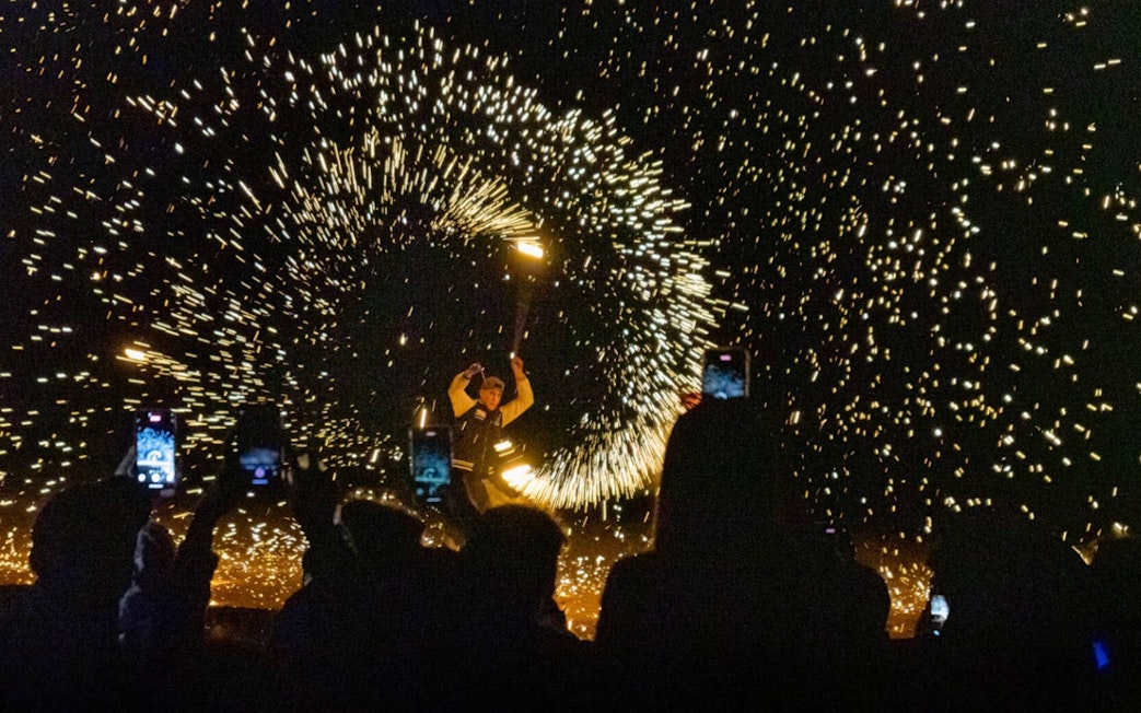 Fire performer at night show in Agafay Desert, Marrakesh with sparks flying.