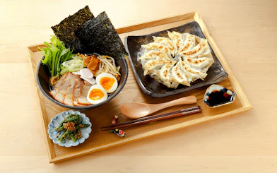 Ramen with sliced pork, soft-boiled eggs, and gyoza on a wooden tray.