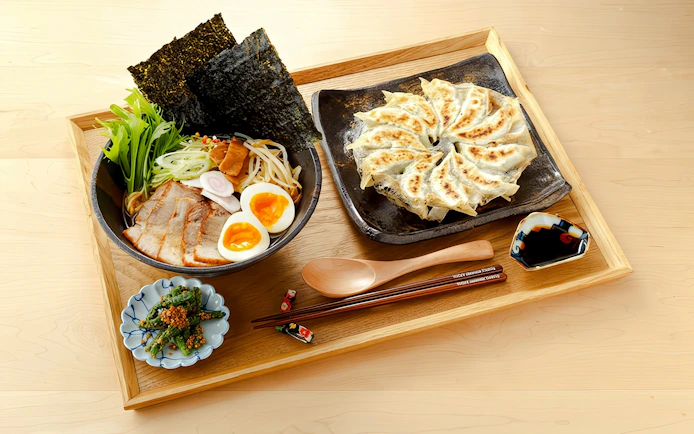 Ramen with sliced pork, soft-boiled eggs, and gyoza on a wooden tray.