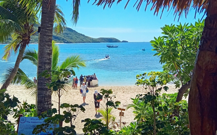 People walking on Kuata Island beach with a marine biologist, Fiji, boat in the background.