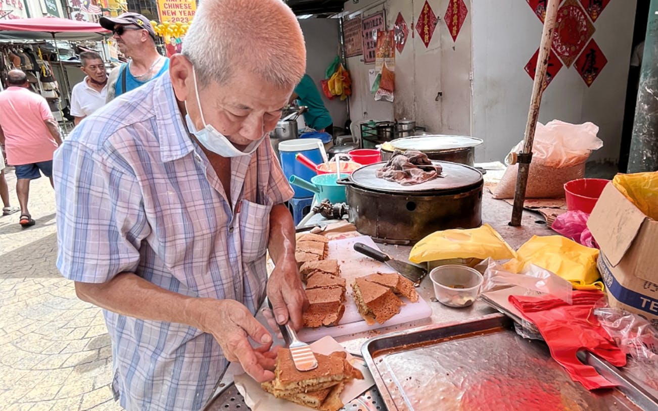 Vendor preparing traditional street food in Kuala Lumpur market.