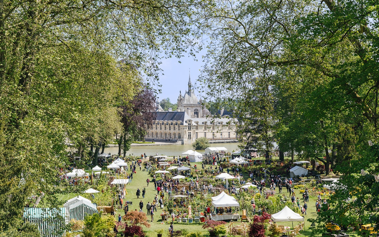Chateau of Chantilly gardens with visitors and market stalls, France.