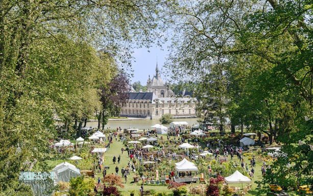 Chateau of Chantilly gardens with visitors and market stalls, France.