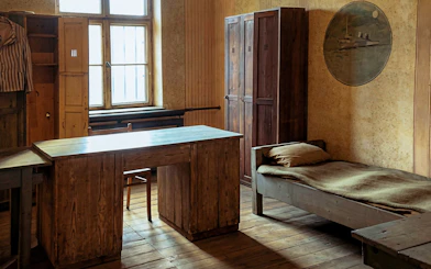 Barracks room interior with wooden bed, desk, and wardrobe at Auschwitz-Birkenau.