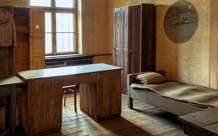 Barracks room interior with wooden bed, desk, and wardrobe at Auschwitz-Birkenau.