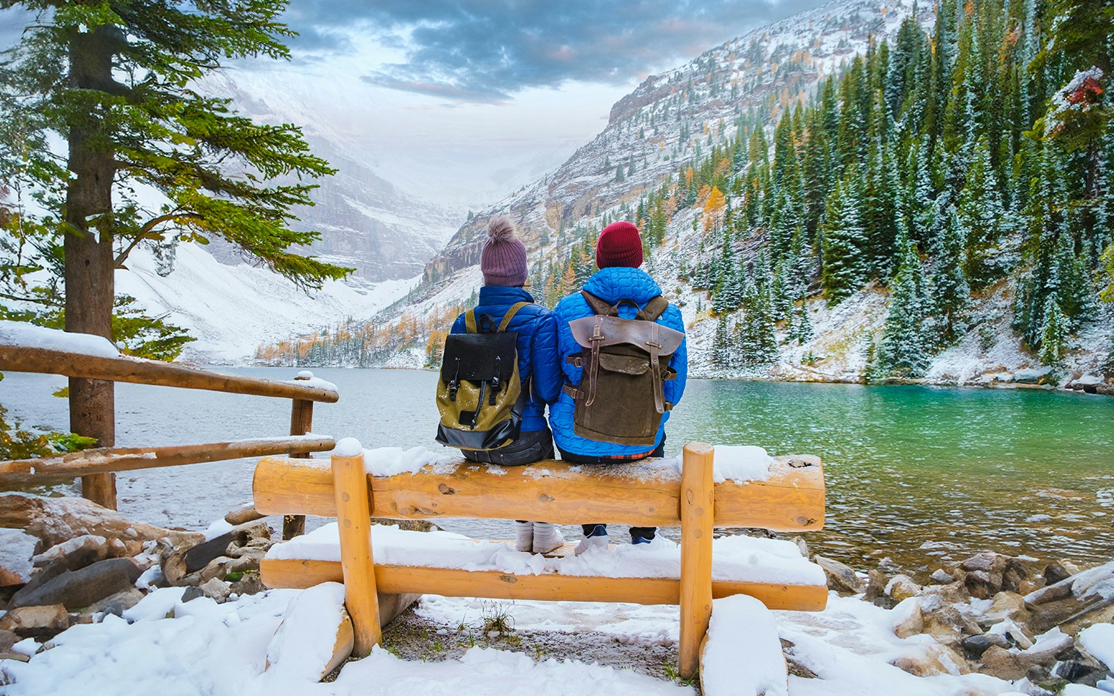 Couple sitting on a bench overlooking Lake Louise with snowy mountains in Banff National Park, Canada.