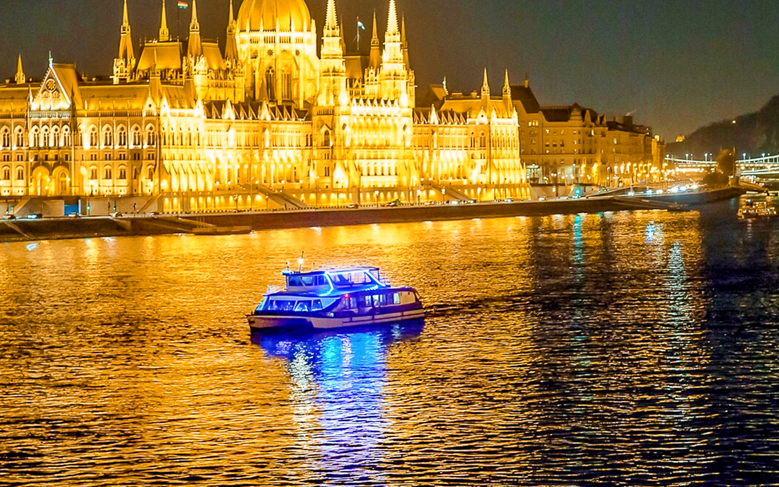 Cruise boat on the Danube River with Budapest Parliament illuminated at night.