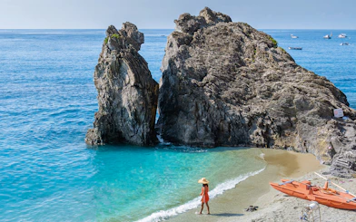 Woman walking on Monterosso beach, Cinque Terre, near large rock formations.