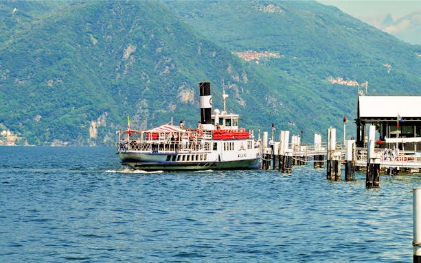Ferry departing from dock on Lake Como with mountains in the background.