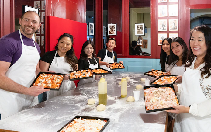 Participants in a Rome kitchen cooking class holding trays of prepared pizza dough.