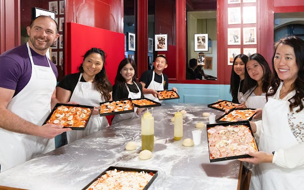 Participants in a Rome kitchen cooking class holding trays of prepared pizza dough.