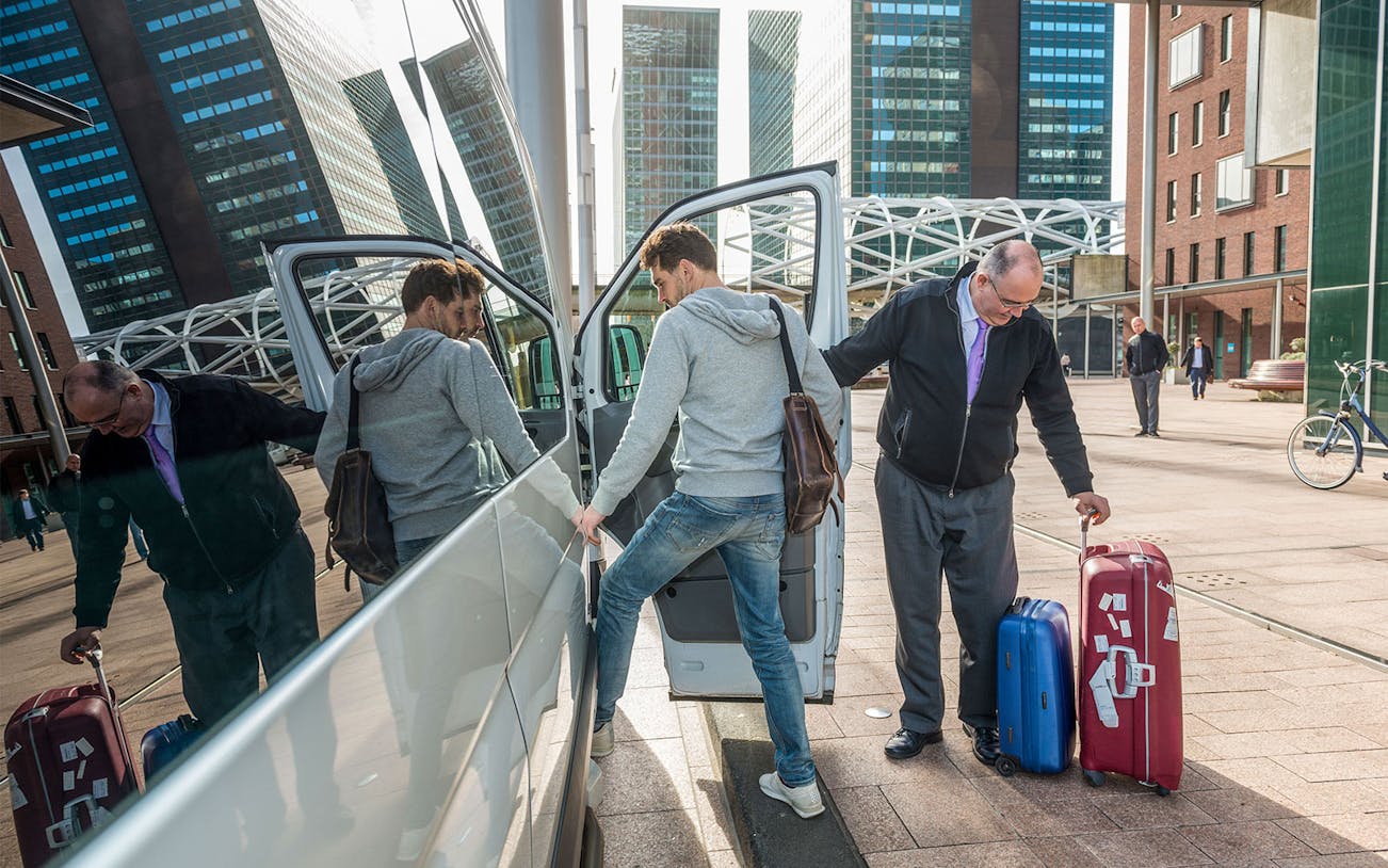 Passengers boarding a shuttle with luggage at an airport transfer location.