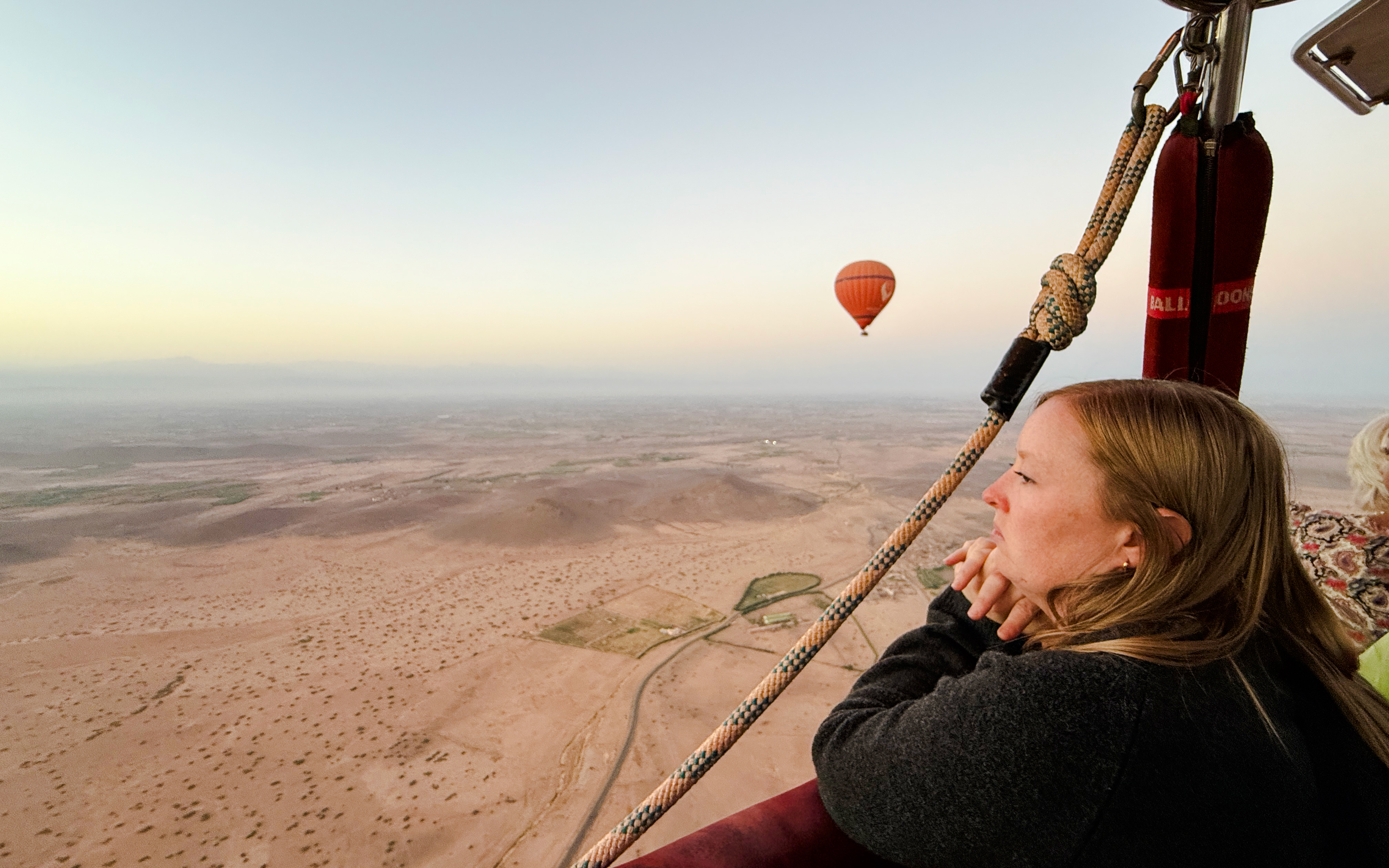 Woman enjoying hot air balloon ride over Marrakech landscape.