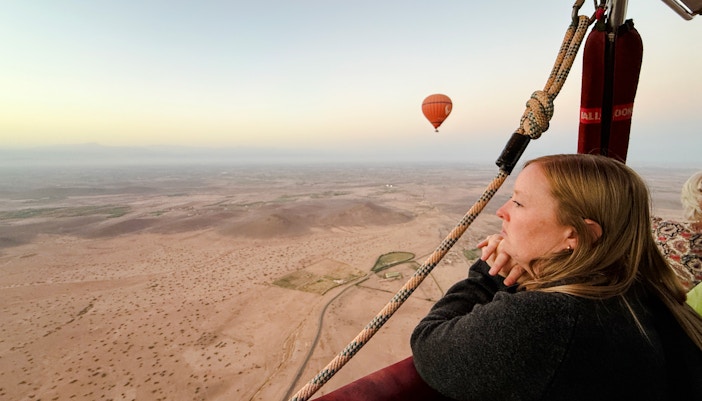 Woman enjoying hot air balloon ride over Marrakech landscape.