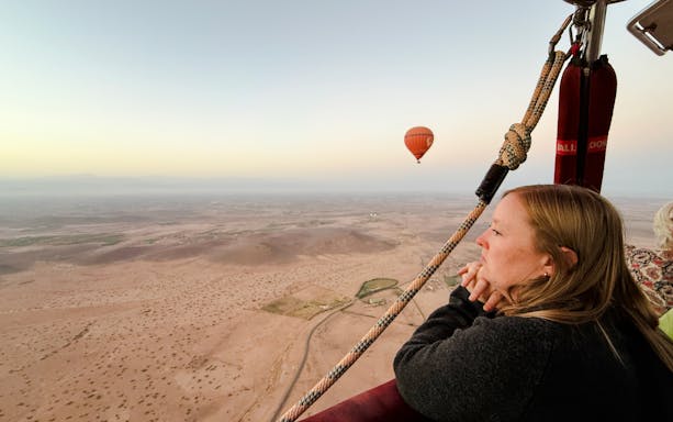 Woman enjoying hot air balloon ride over Marrakech landscape.