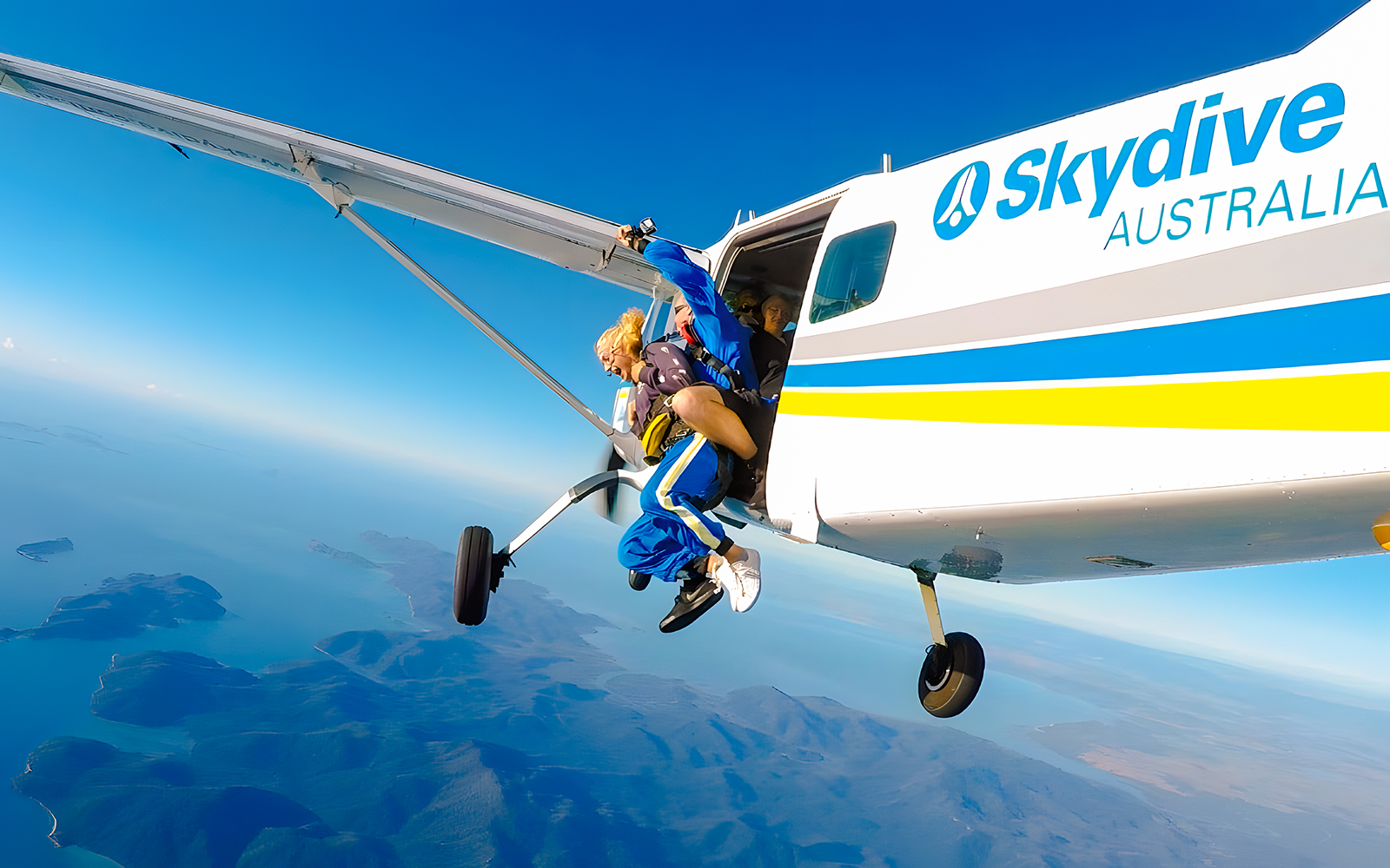 Tandem skydiving over Airlie Beach, instructor and skydiver exiting plane.
