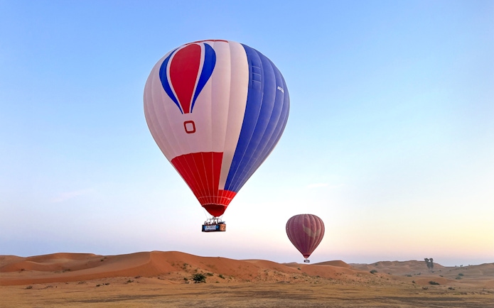 Hot air balloons floating over desert at sunrise in Ras Al Khaimah.