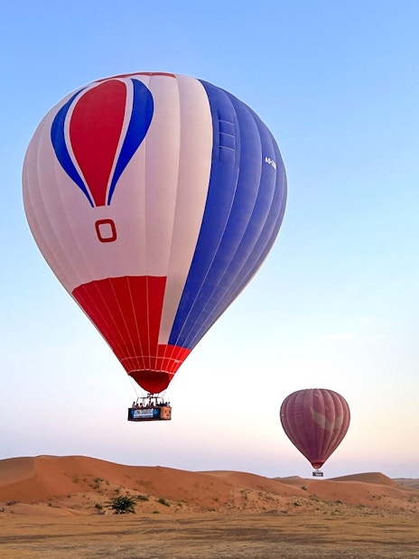 Hot air balloons floating over desert at sunrise in Ras Al Khaimah.