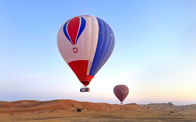 Hot air balloons floating over desert at sunrise in Ras Al Khaimah.
