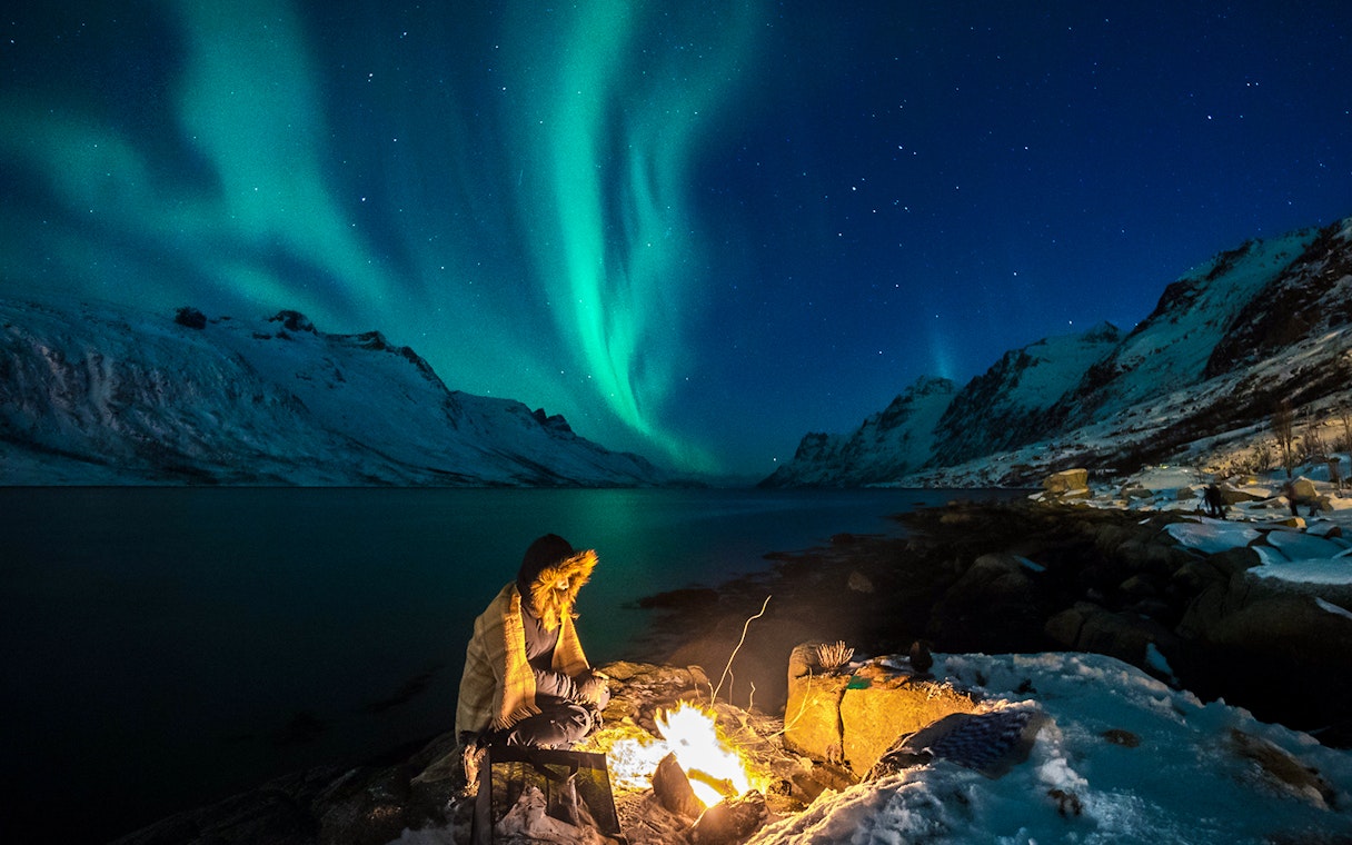 Person by campfire under Northern Lights in Tromsø, Norway.