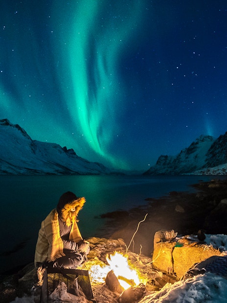 Person by campfire under Northern Lights in Tromsø, Norway.