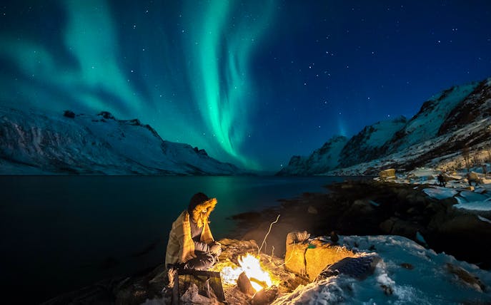 Person by campfire under Northern Lights in Tromsø, Norway.