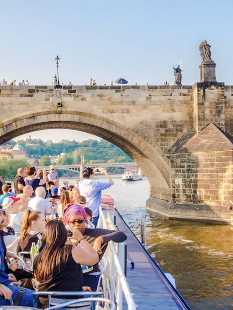 Sightseeing cruise under Charles Bridge in Prague with tourists on deck.