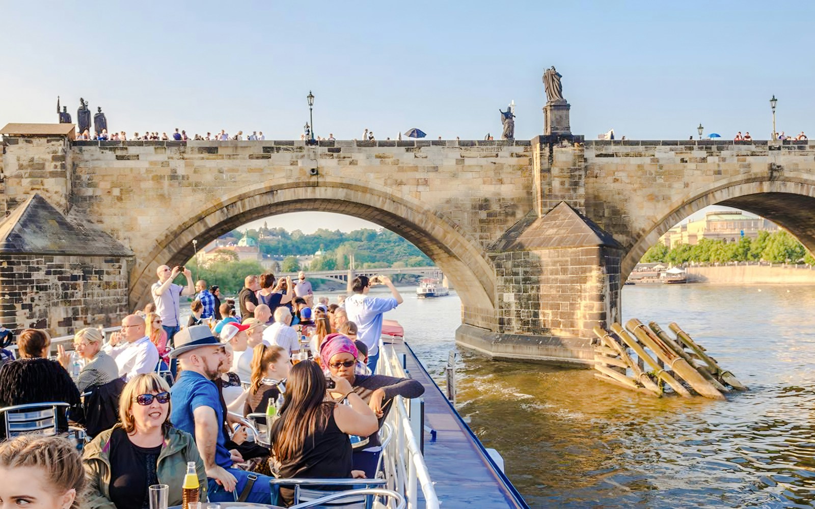 Sightseeing cruise under Charles Bridge in Prague with tourists on deck.