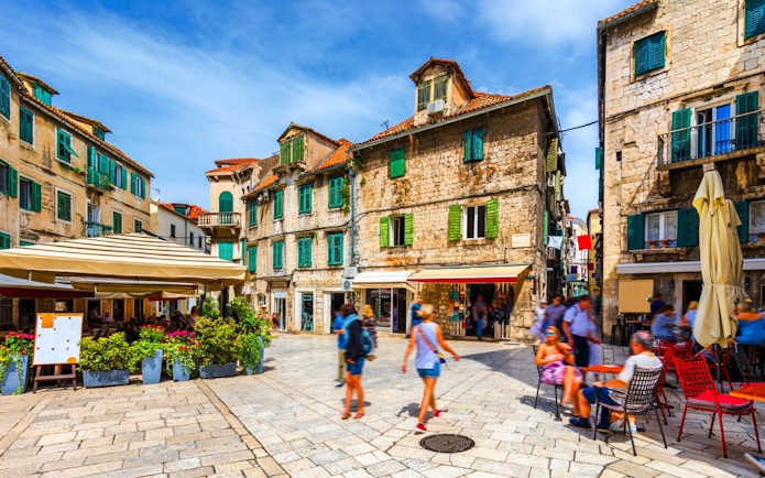 Old town square in Split, Croatia with historic stone buildings and people enjoying outdoor cafes.