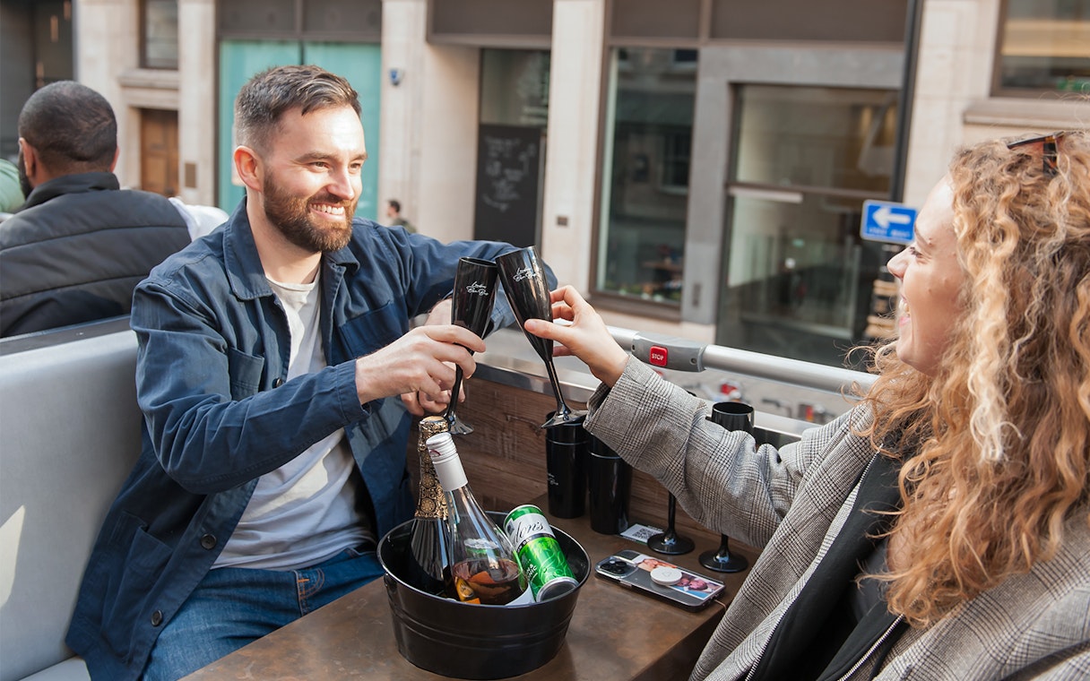 Man and woman toasting drinks on an open-top bus tour.