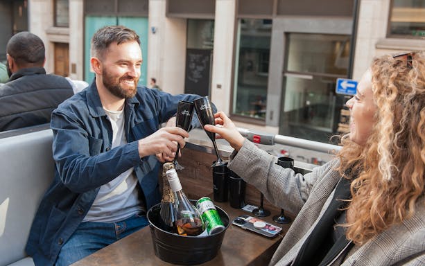 Man and woman toasting drinks on an open-top bus tour.