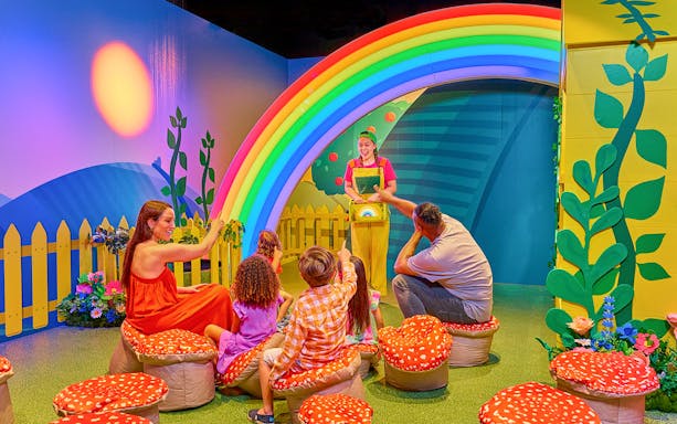 Children and adults enjoying CBeebies Rainbow Adventure under a colorful rainbow arch.