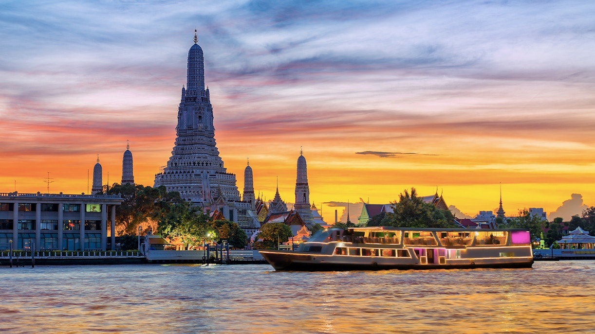 Cruise boat on Chao Phraya River with Wat Arun temple at sunset, Bangkok.