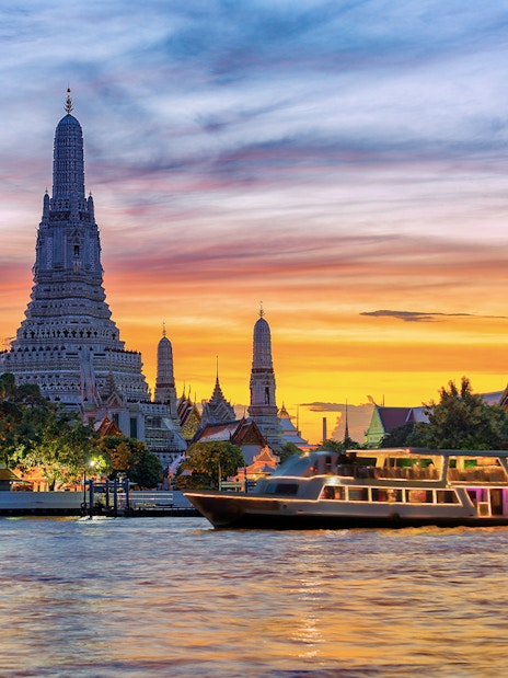 Cruise boat on Chao Phraya River with Wat Arun temple at sunset, Bangkok.