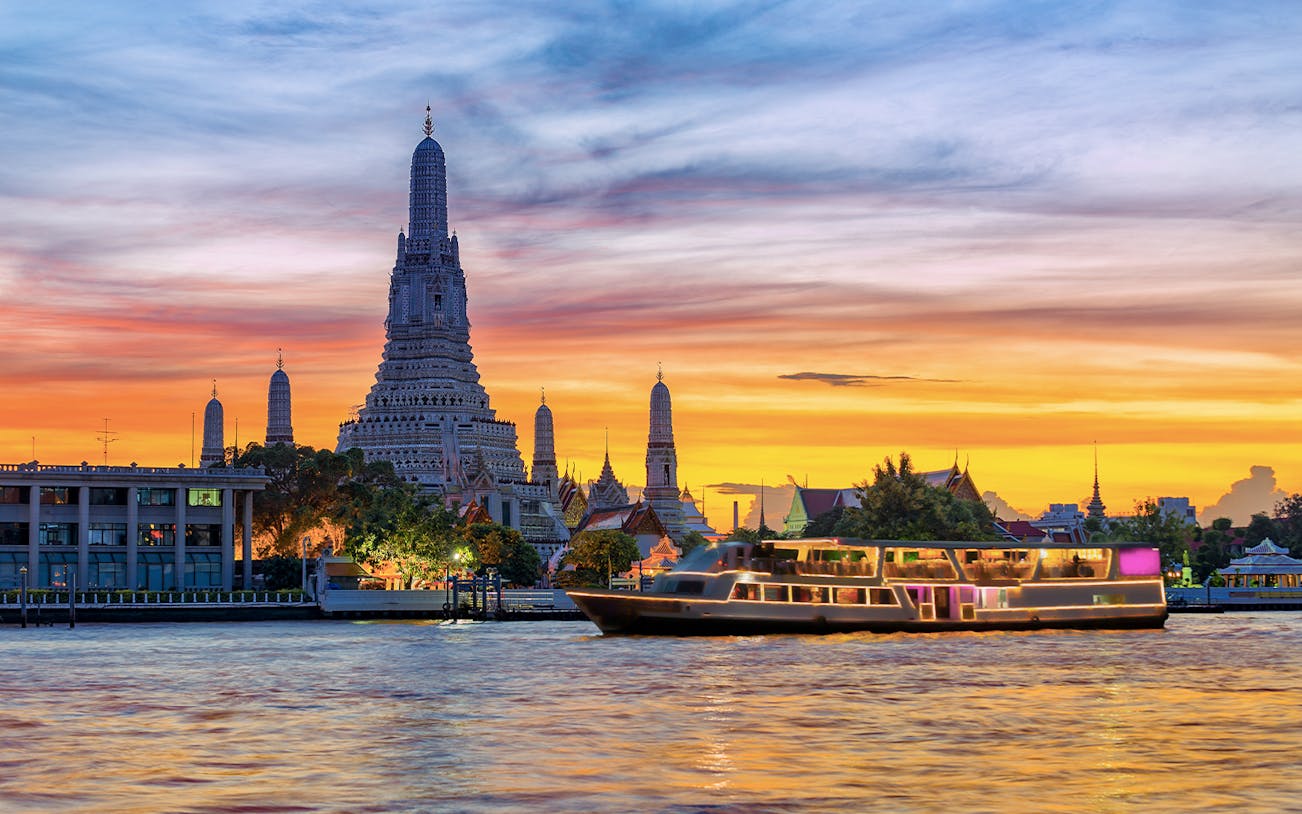 Cruise boat on Chao Phraya River with Wat Arun temple at sunset, Bangkok.