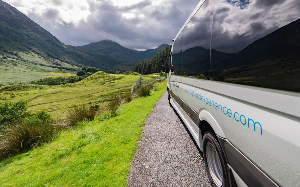 Transfer vehicle on scenic route through Scottish Highlands.