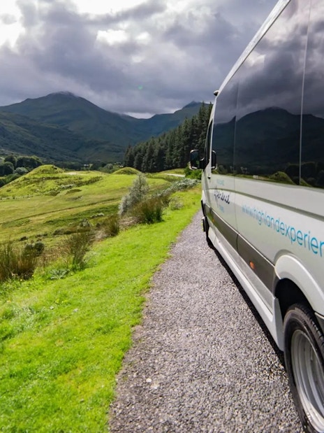 Transfer vehicle on scenic route through Scottish Highlands.