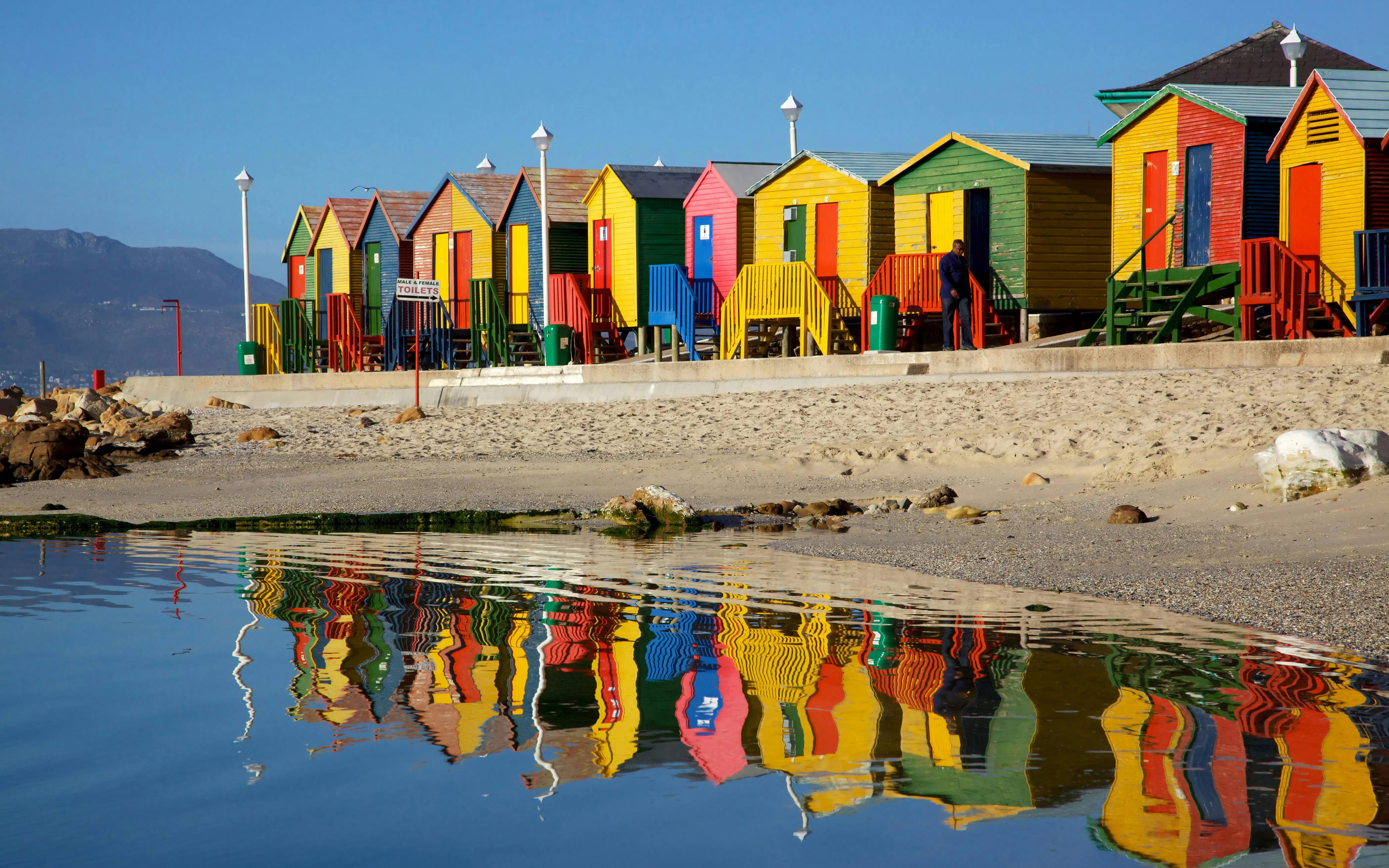 Brightly colored beach huts at St James, Cape Town, reflecting in the water.