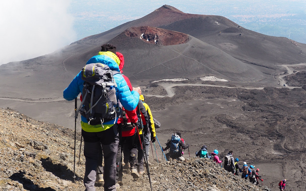 Hikers descending Mount Etna with summit crater in view, Sicily.