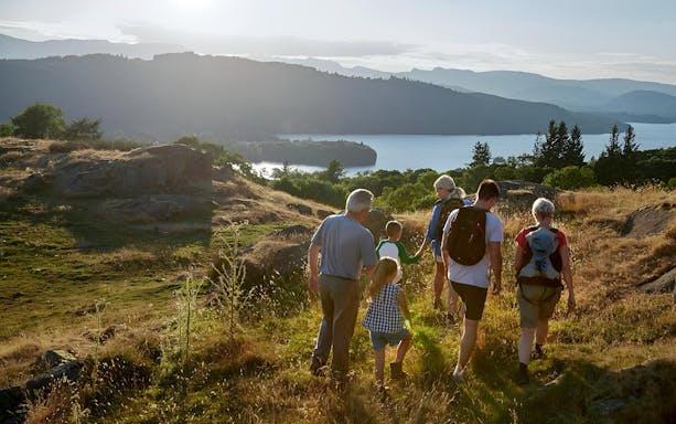 Group hiking in the Lake District with scenic lake and hills in the background.